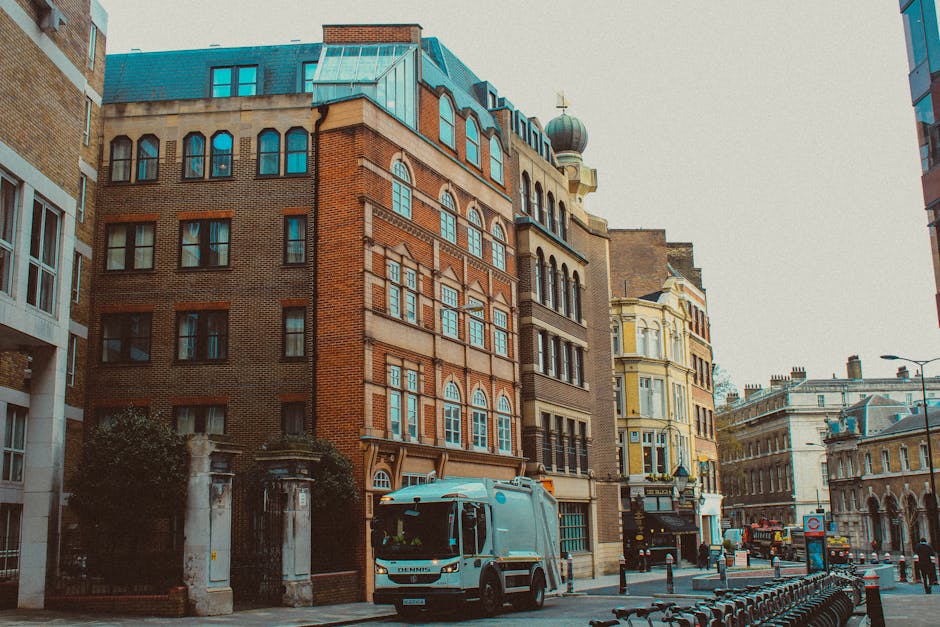 A silver moving van parked on a city street next to a historic brick building with large windows and stone detailing around the door. The van faces slightly away from the camera, positioned close to t